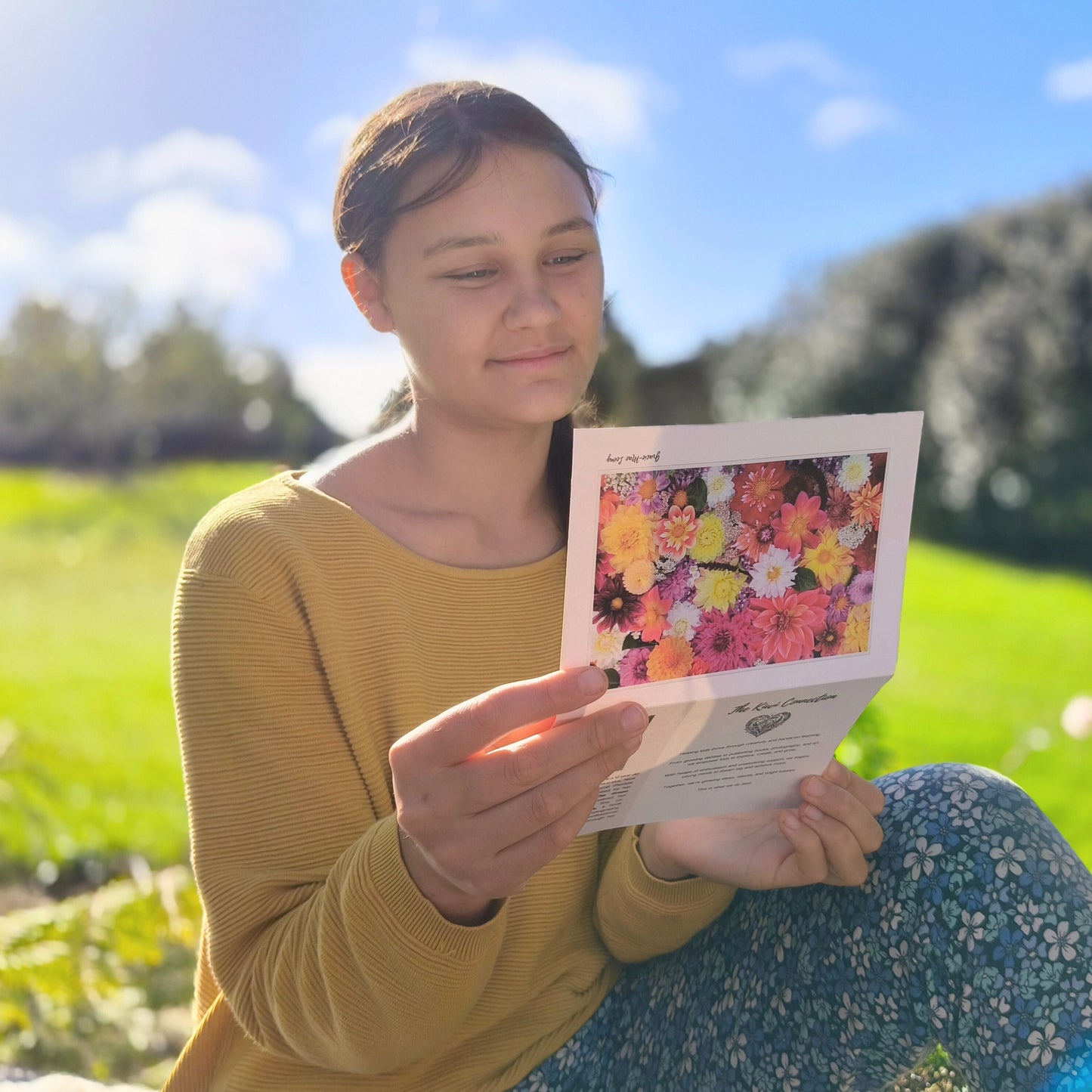 Woman holding a colorful floral card in a field with a blue sky.