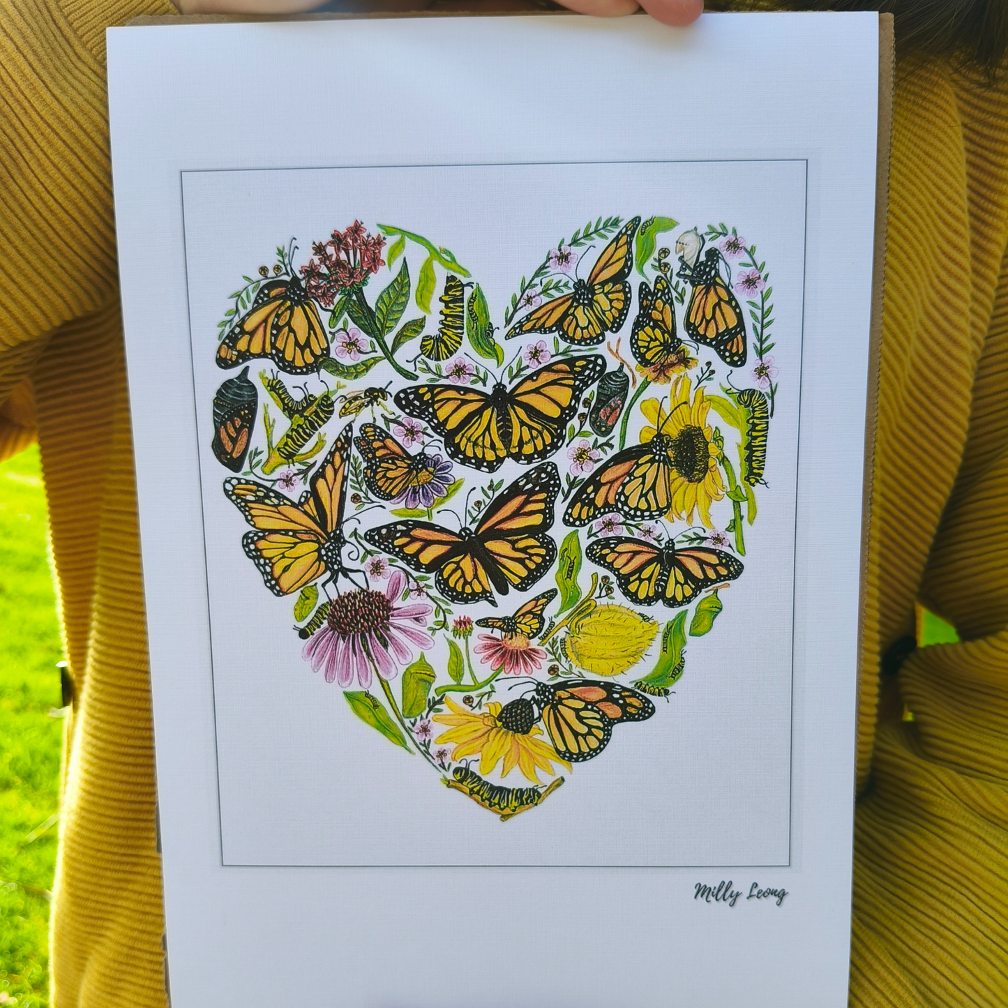Heart-shaped design with butterflies and flowers held by a person wearing a yellow sweater.