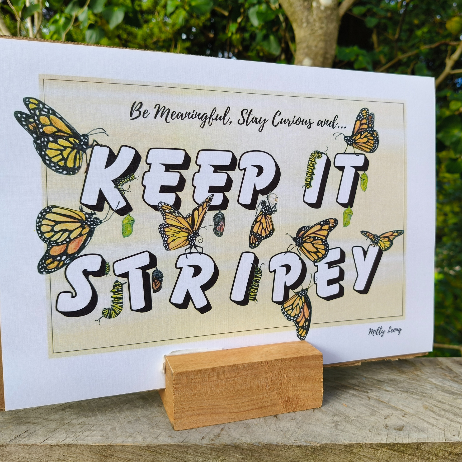 A4 art print with butterflies and text 'KEEP IT STRIPEY' on a wooden stand outdoors.