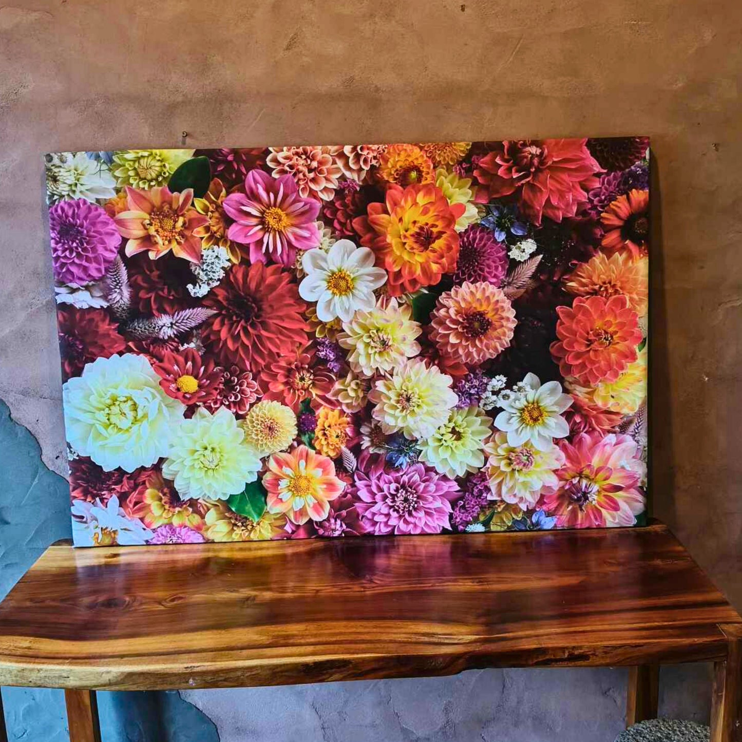 A large floral canvas of multi coloured dahlias on a wooden table in teh sunshine.